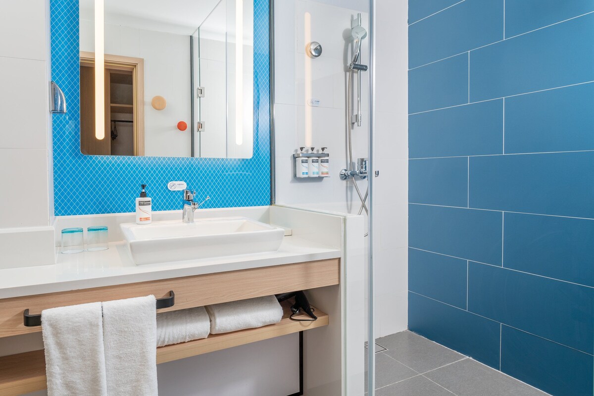 A modern bathroom with a white sink, blue-tiled shower, and a wooden vanity.