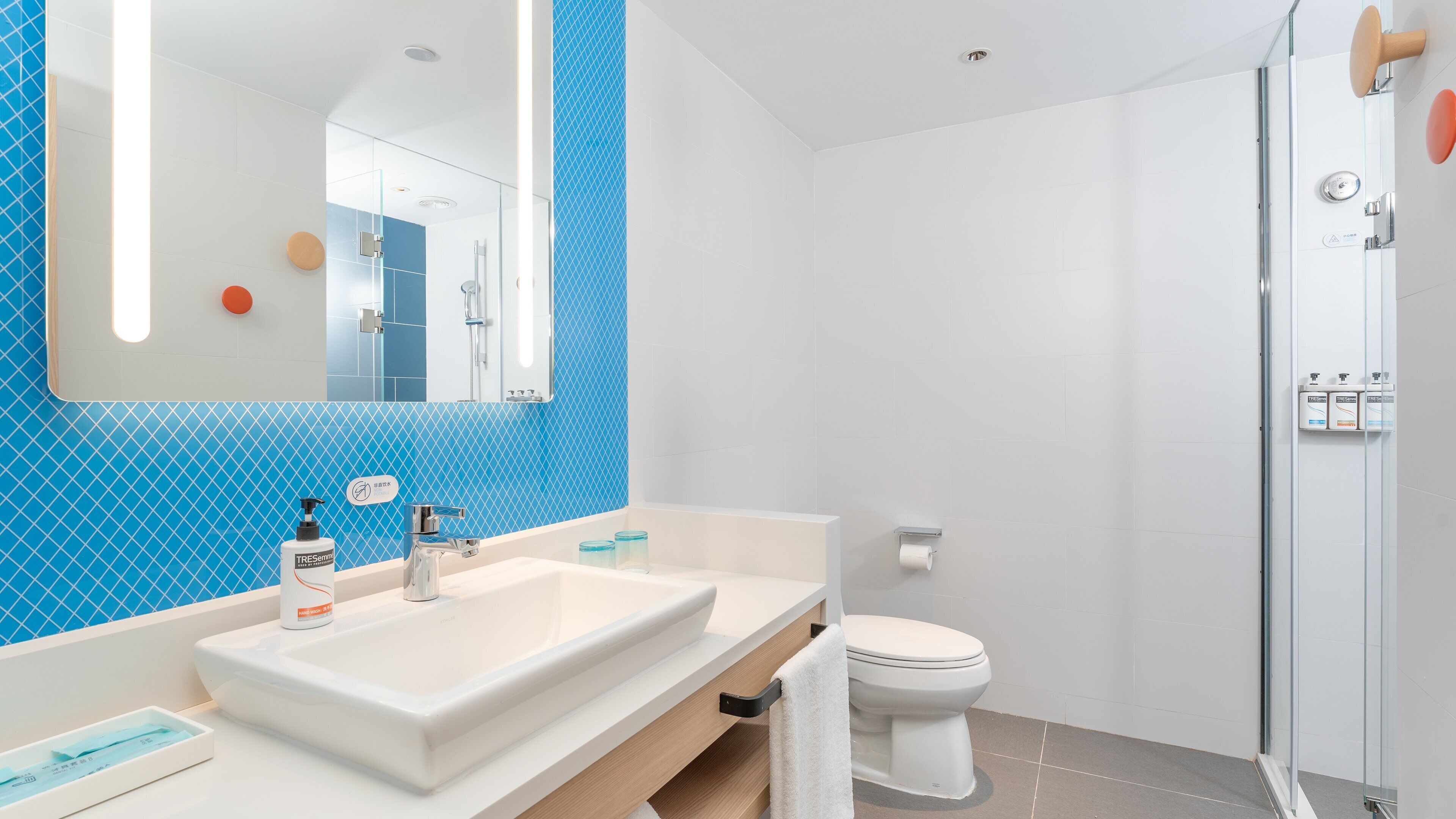 Een moderne badkamer met een grote spiegel, twee wasbakken, een toilet en een douchehoek.