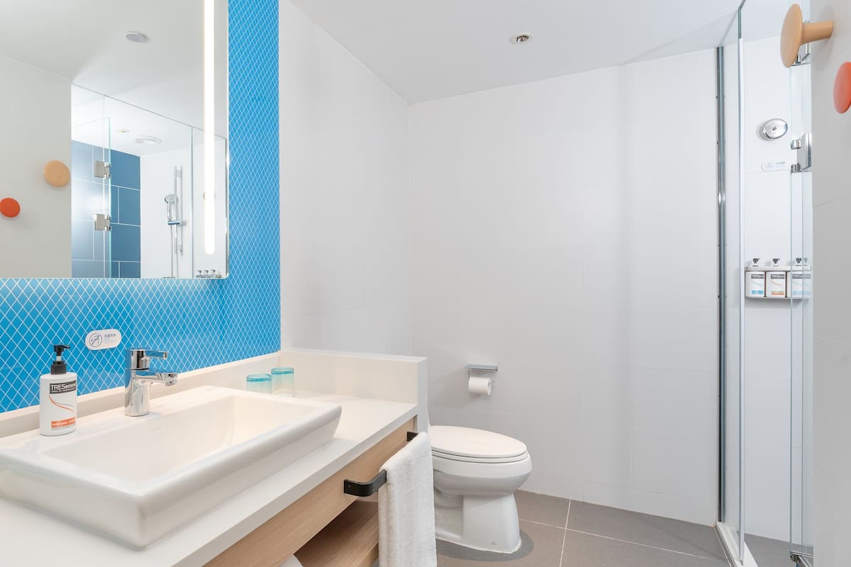 A modern bathroom with a large mirror, two sinks, a toilet, and a shower area.