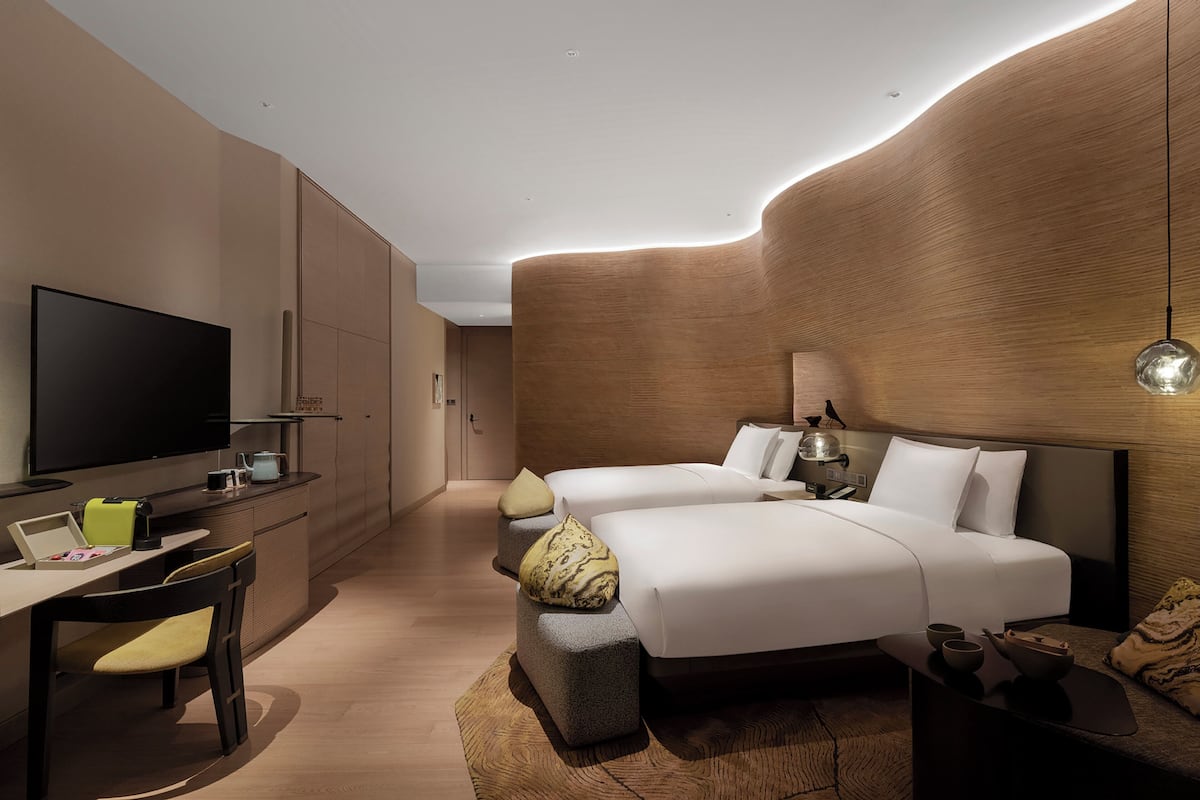 Une chambre d’hôtel moderne dotée d’une télévision à écran plat, d’un bureau avec un ordinateur portable, de deux lits avec une literie blanche et d’un mur décoratif en bois.