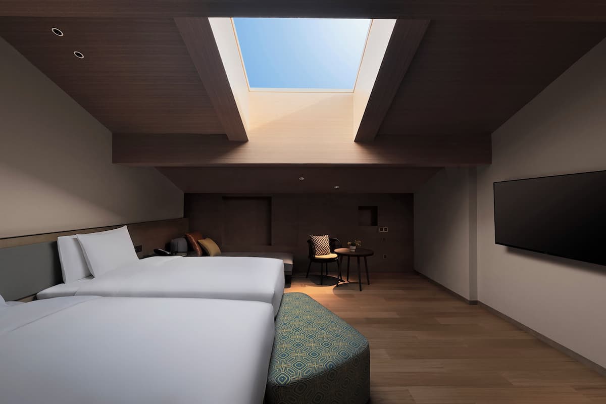 Une chambre moderne avec une lucarne, deux lits, un canapé, une petite table et un téléviseur.