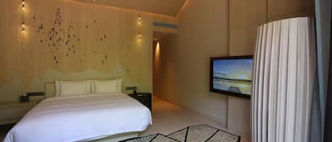 Una habitación de hotel moderna con una cama grande, un televisor de pantalla plana montado en la pared y una alfombra con un diseño geométrico original.