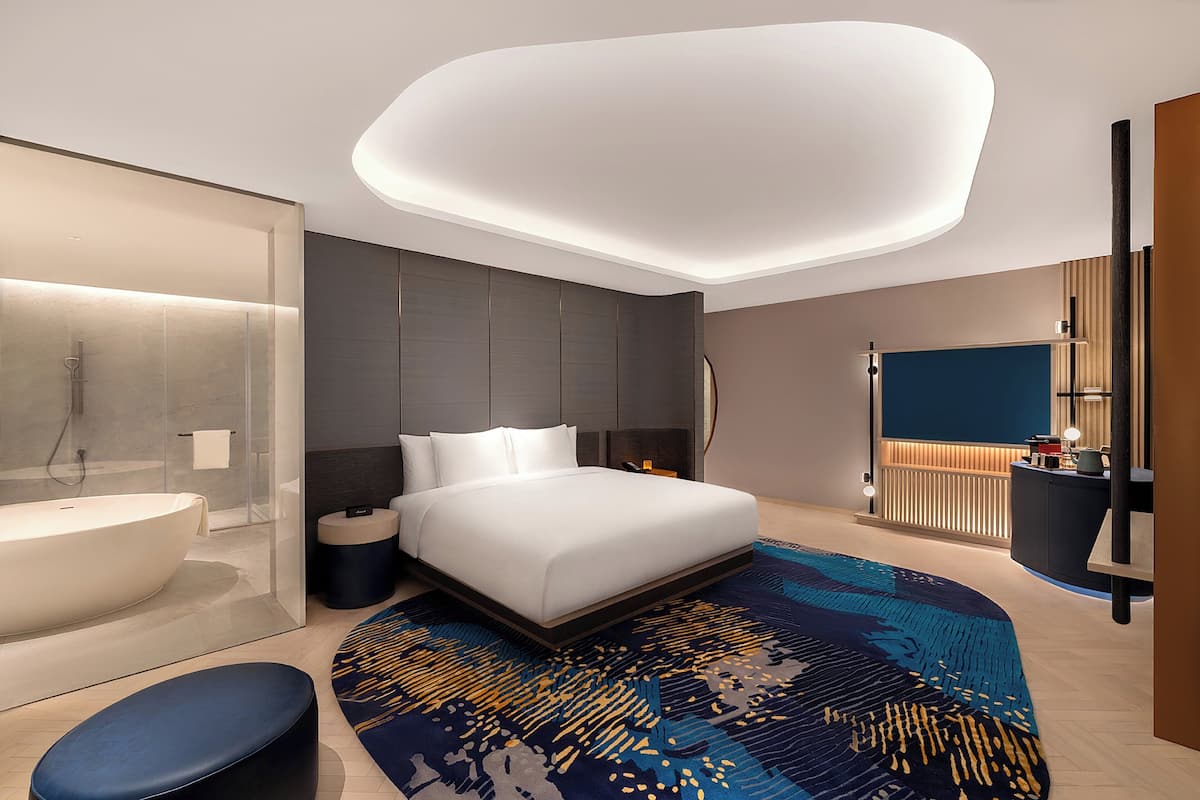 Une chambre d’hôtel moderne dotée d’un grand lit, d’une salle de bain séparée, d’un bureau et d’un grand miroir.