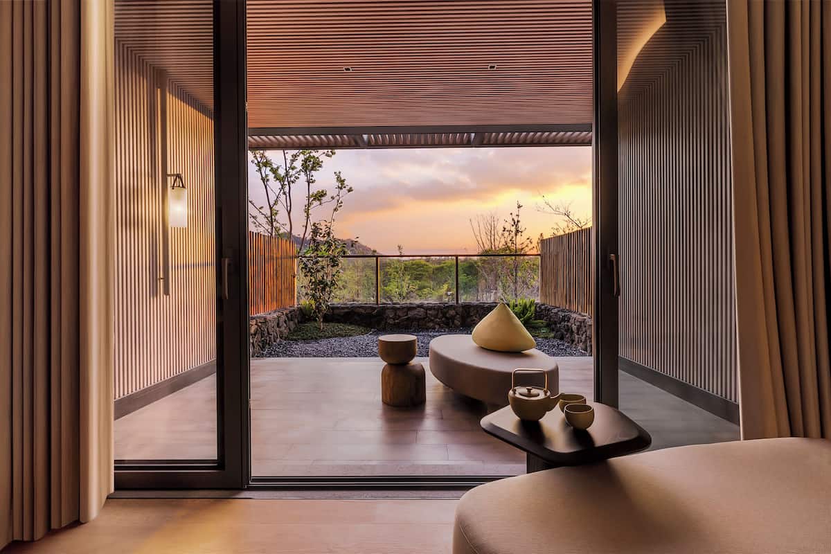 Un intérieur moderne avec une porte-fenêtre coulissante donnant sur un patio extérieur aménagé dans un style minimaliste et offrant une vue sur le coucher du soleil.