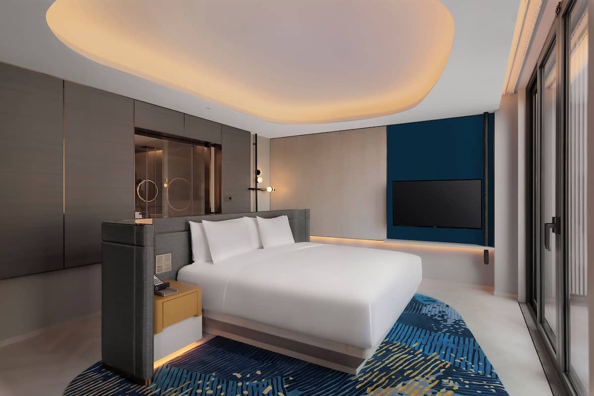 Une chambre d’hôtel moderne dotée d’un grand lit, d’une table de chevet, d’un téléviseur intégré et d’une grande fenêtre.
