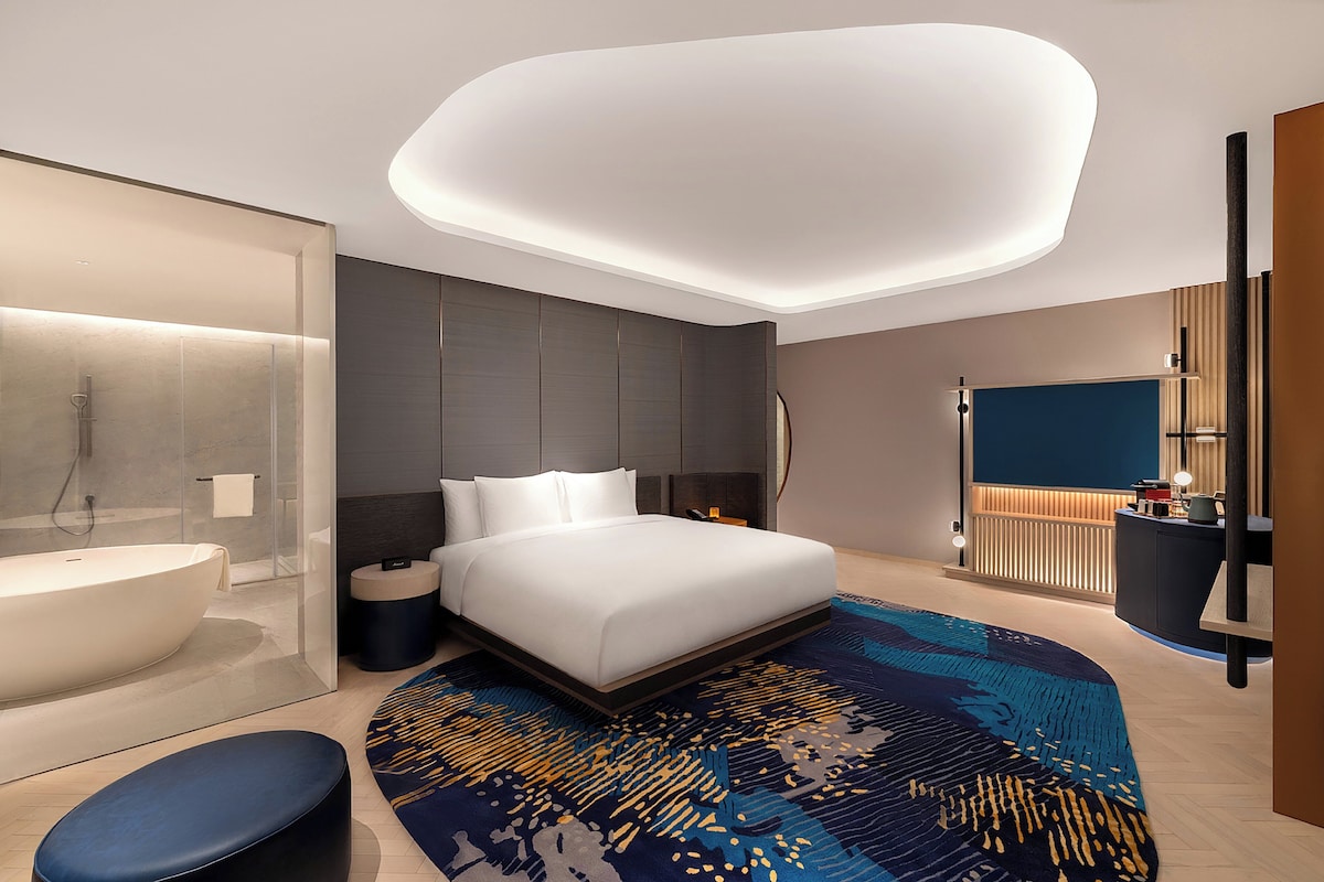 Une chambre d’hôtel moderne dotée d’un grand lit, d’une salle de bain séparée, d’un bureau et d’un grand miroir.