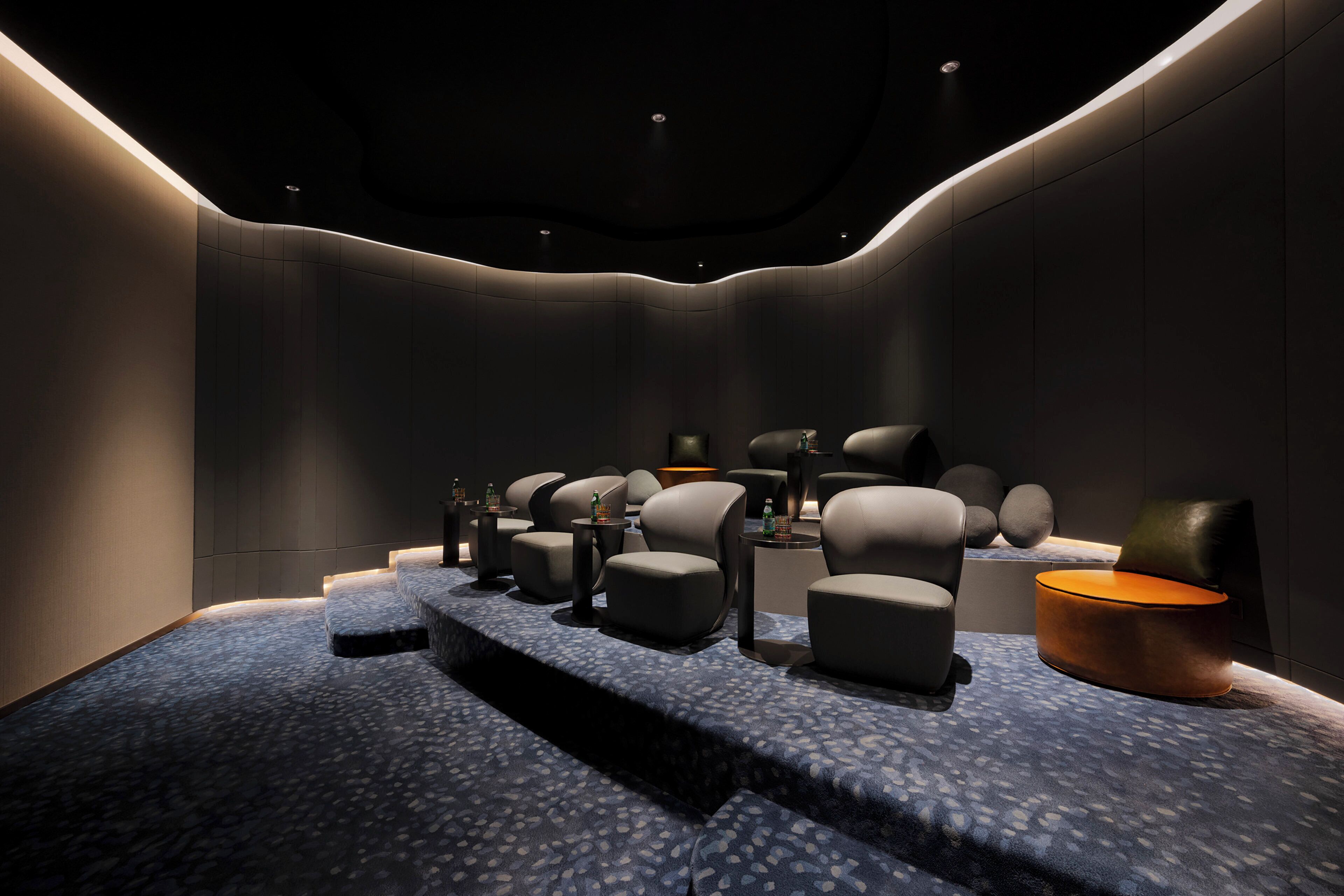 A modern cinema room with tiered seating, ambient lighting, and a dark interior.