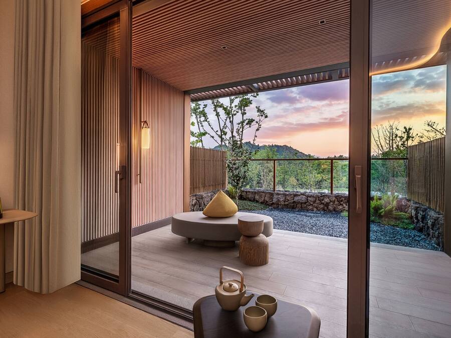 Un interior moderno con un divisor corredizo de vidrio que da a un balcón con vistas panorámicas de colinas y un atardecer.