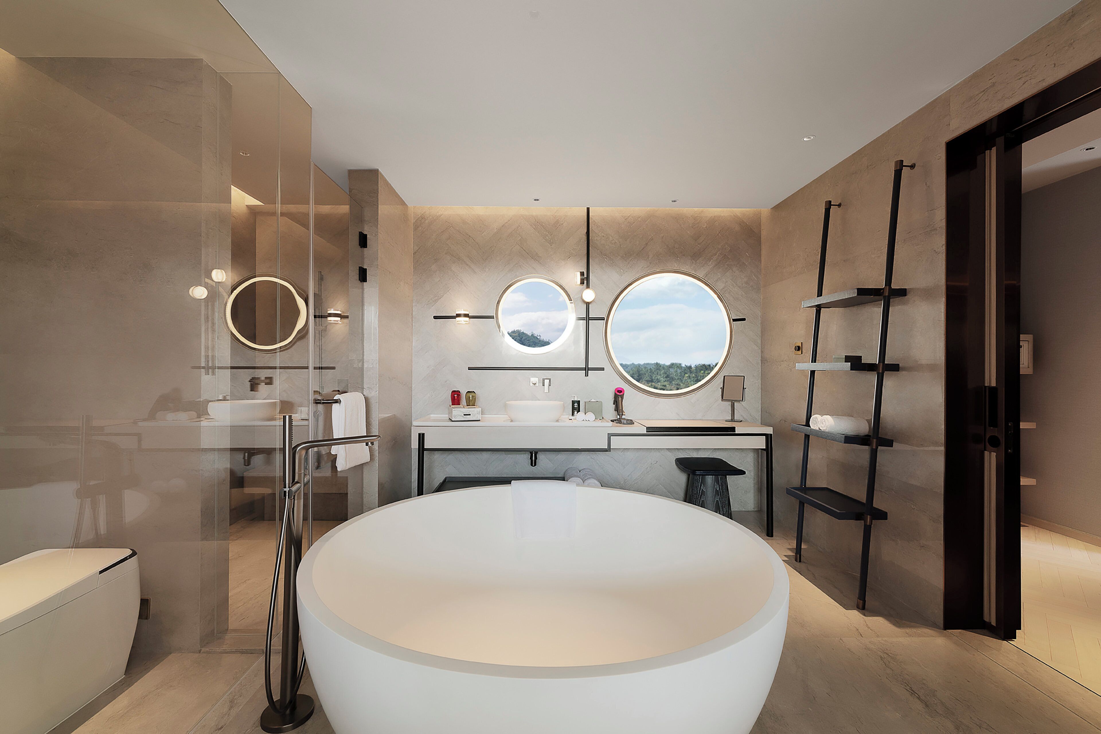 A modern bathroom with a large bathtub, two round mirrors, and a vanity with a sink and countertop.