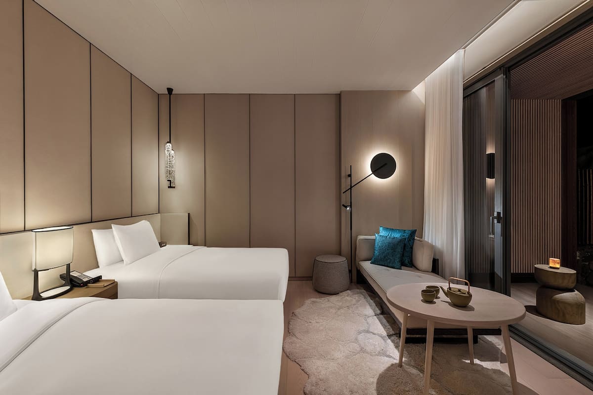 Une chambre d’hôtel moderne avec deux lits, un canapé, une petite table et une table de chevet.