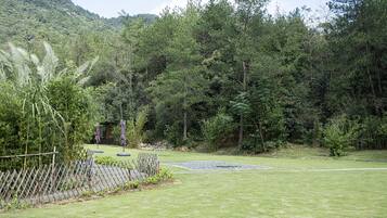 Un jardín cuidado con un cerramiento de madera, un pequeño estanque y un bosque denso al fondo.