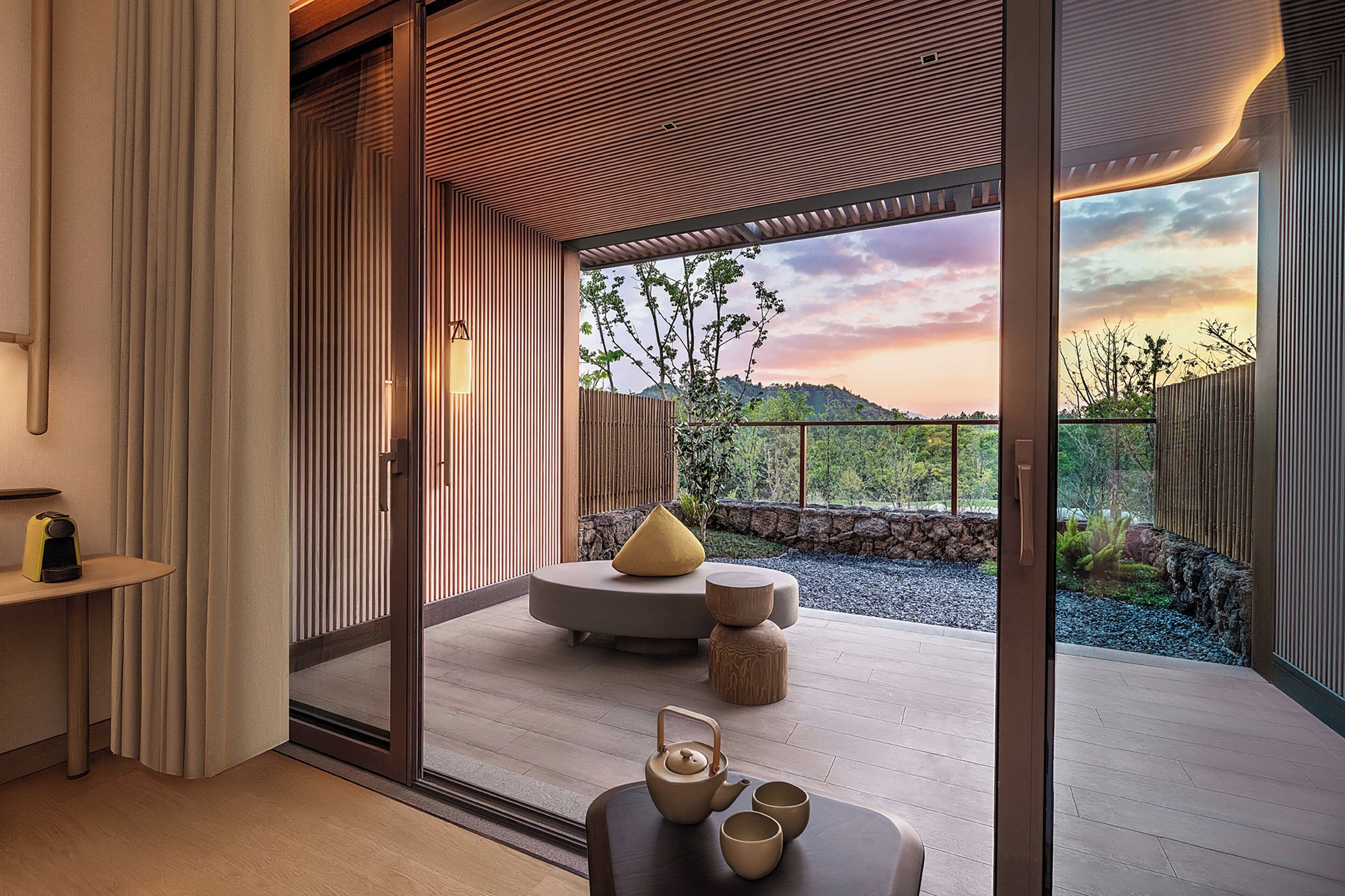 A modern interior with a sliding glass door leading to a balcony with a view of trees and hills.