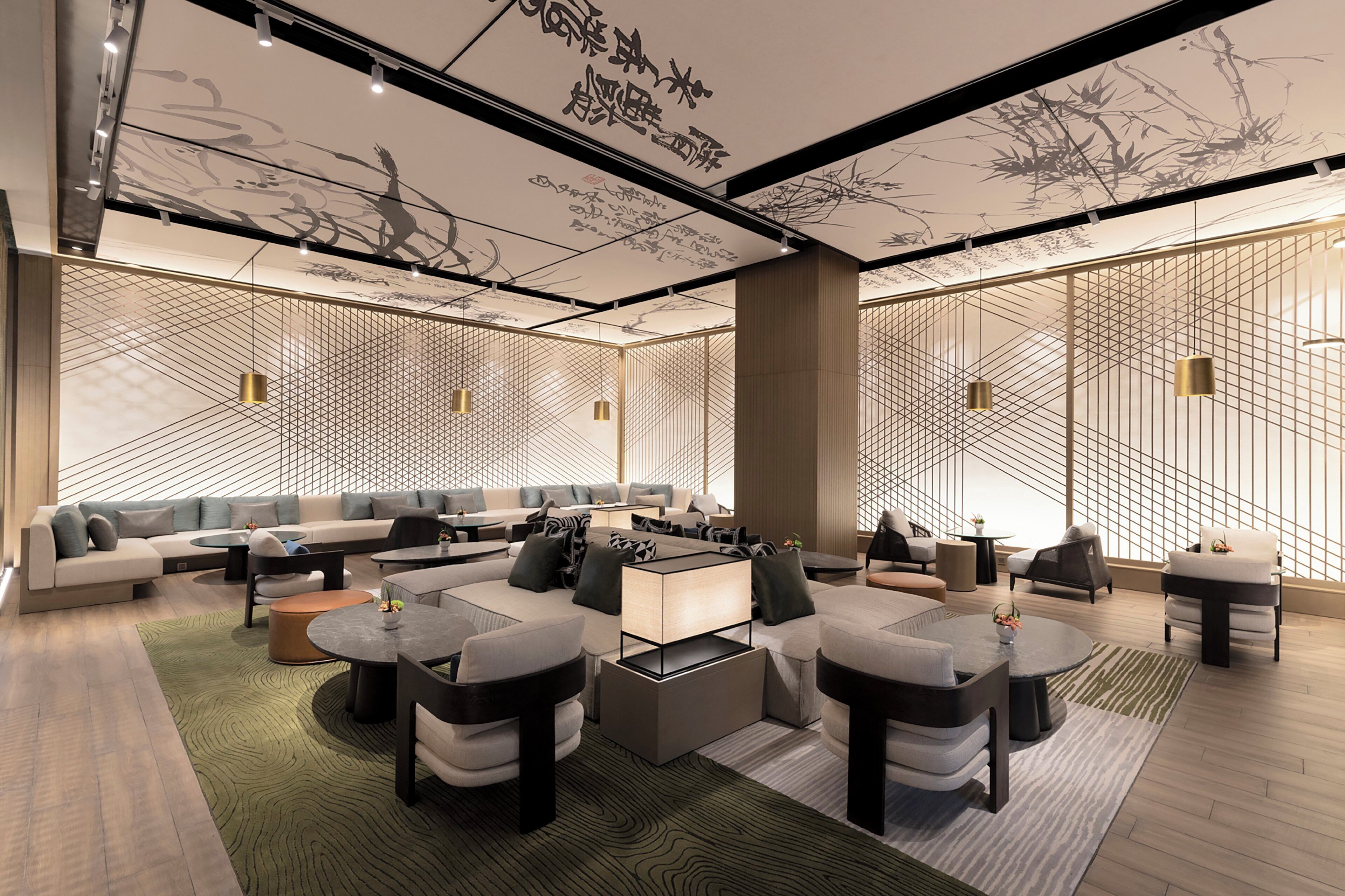 A modern lounge area with a sectional sofa, round tables, and a decorative ceiling with calligraphy.