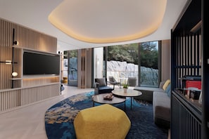 Un salon moderne doté d’un téléviseur à écran plat, de sièges confortables, d’une table basse et de grandes fenêtres offrant une vue sur l’extérieur.
