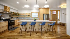 Una cocina moderna con armarios de madera, una isla central con taburetes de bar, electrodomésticos de acero inoxidable e iluminación colgante.
