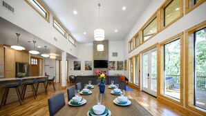 Un comedor amplio con una mesa de madera dispuesta para seis personas, rodeada de sillas. Un jarrón grande con flores se encuentra en el centro.