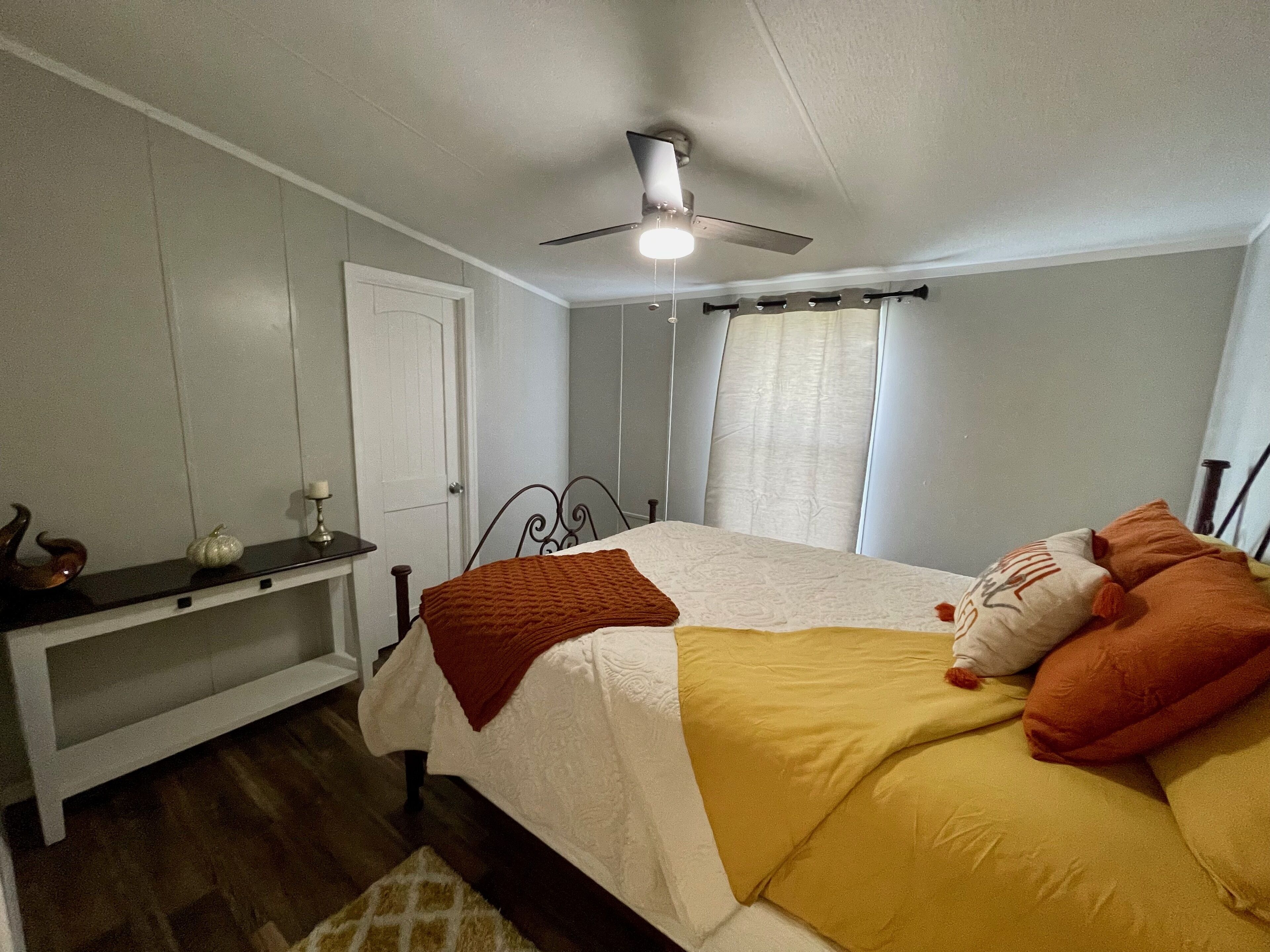 A bedroom with a bed, a nightstand, a ceiling fan, and a window with curtains.