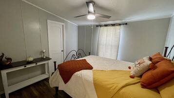 A bedroom with a bed, a nightstand, a ceiling fan, and a window with curtains.