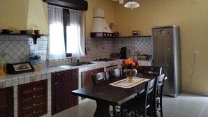 Et køkken med flisebeklædt backsplash, komfur, vask og køleskab. Der er et spisebord med stole og en vase med blomster.