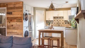 Een knus leefruimte met kitchenette, houten wand, wasmachine en een eethoek met tafel en stoelen.