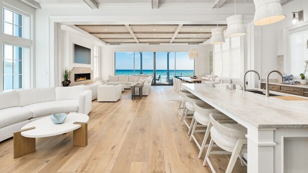 Un amplio salón con un gran ventanal con vistas al océano, una cocina moderna con taburetes de bar y una zona de estar acogedora.