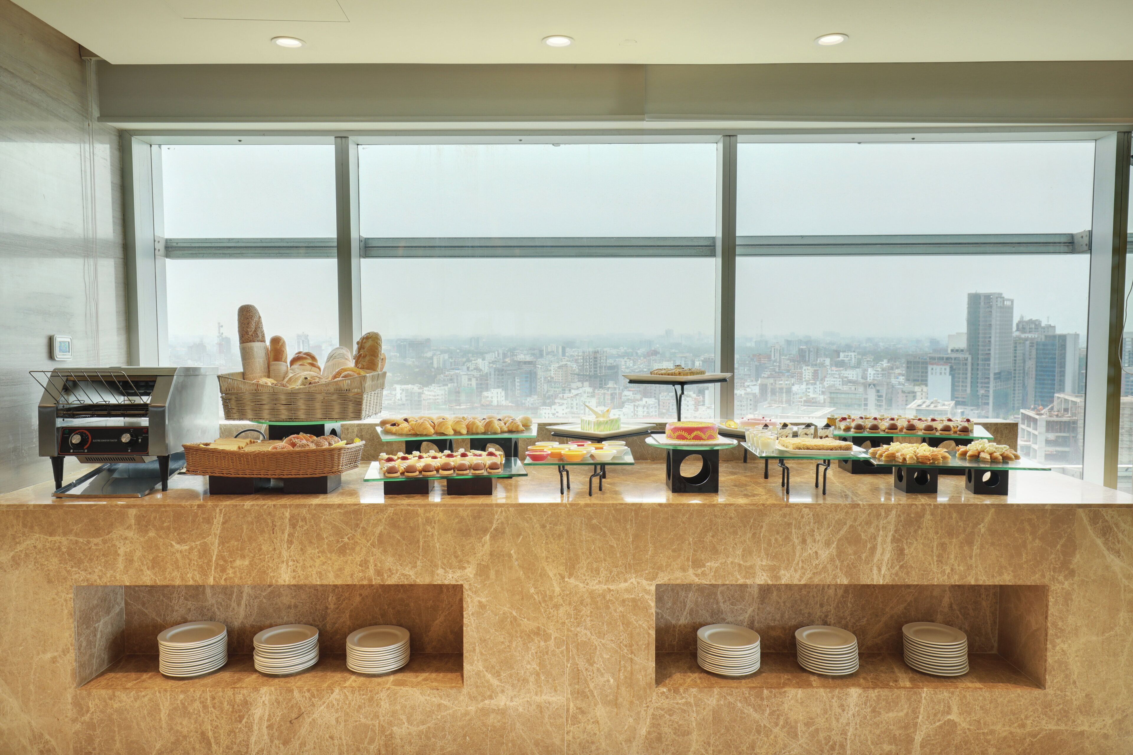 Ein reichhaltiges Buffet mit verschiedenen Speisen und Blick auf eine Stadtlandschaft durch große Fenster.