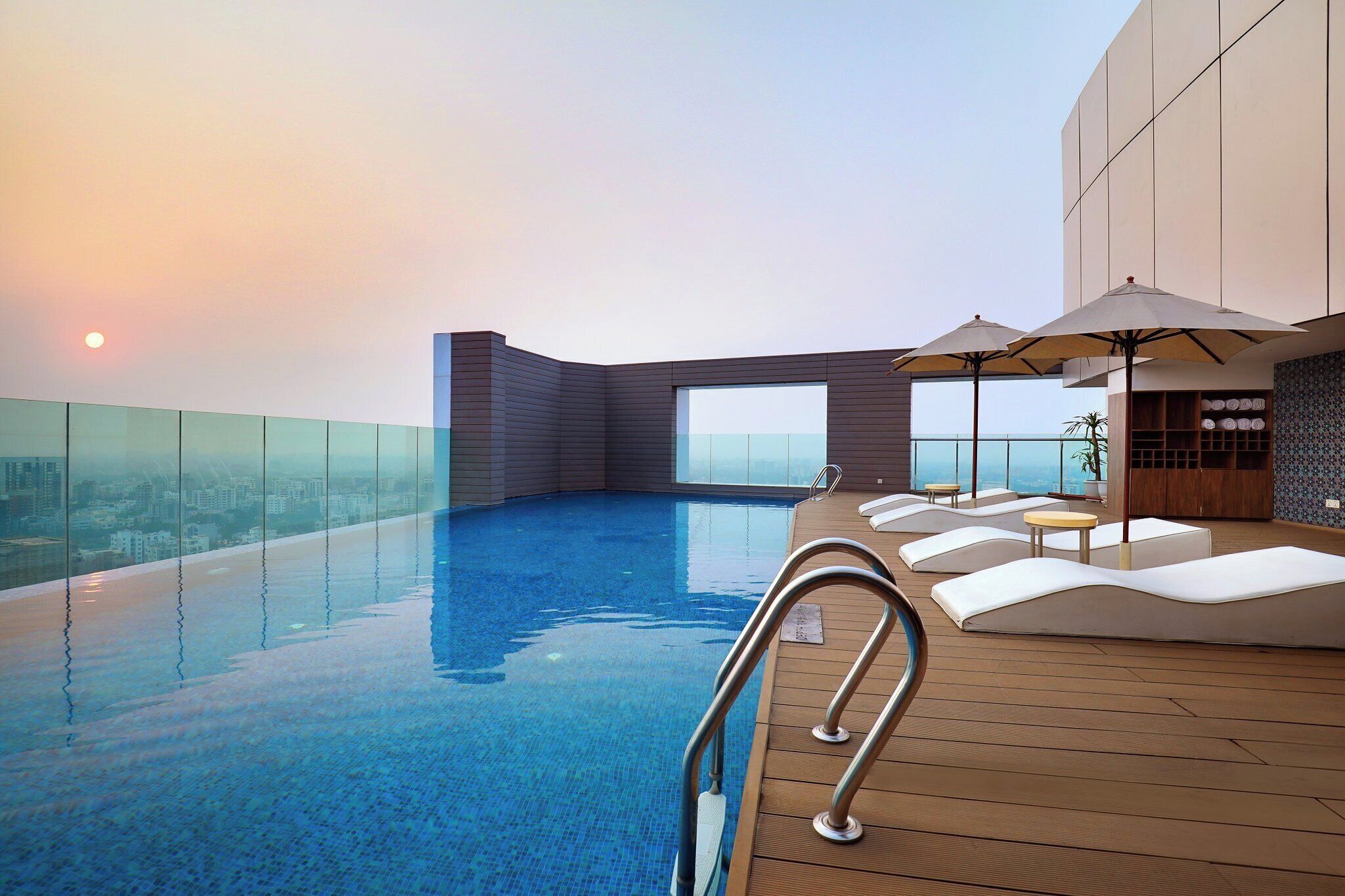 A rooftop infinity pool with a view of the city skyline, lounge chairs, and umbrellas.