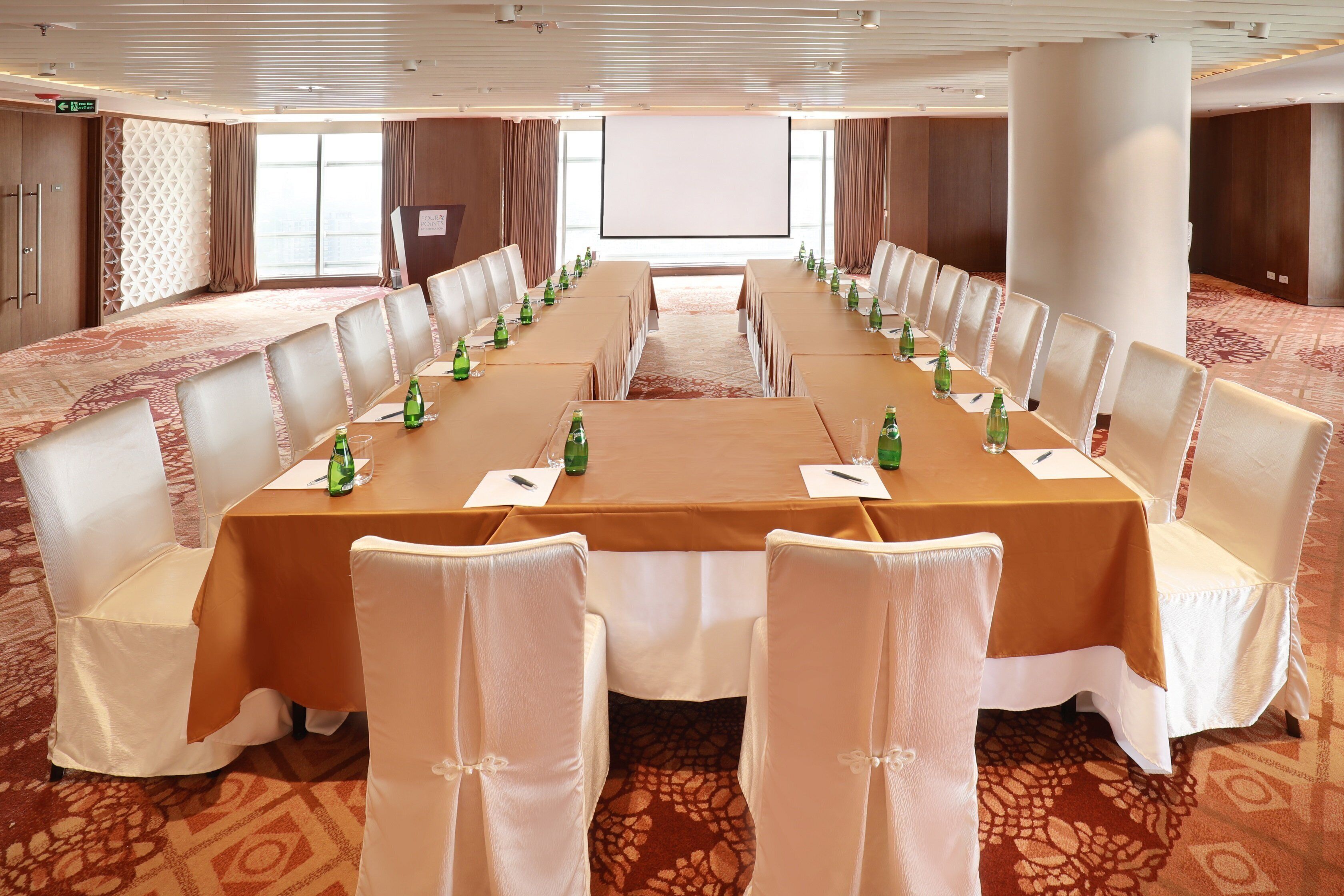 A conference room with a long table, chairs, and a projector screen.