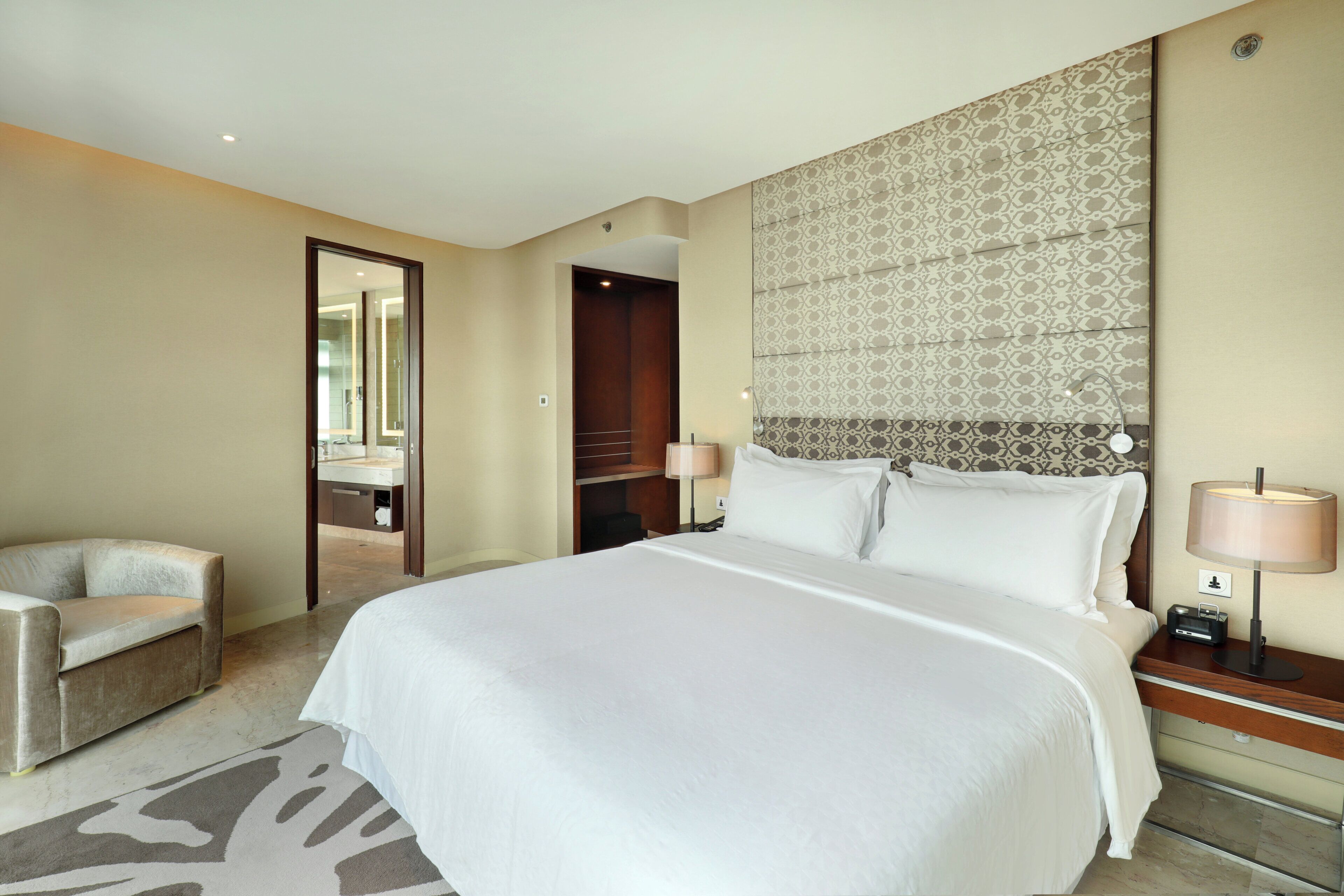 Una habitación de hotel con una cama grande, una mesita de noche con lámpara, una silla y un espejo.
