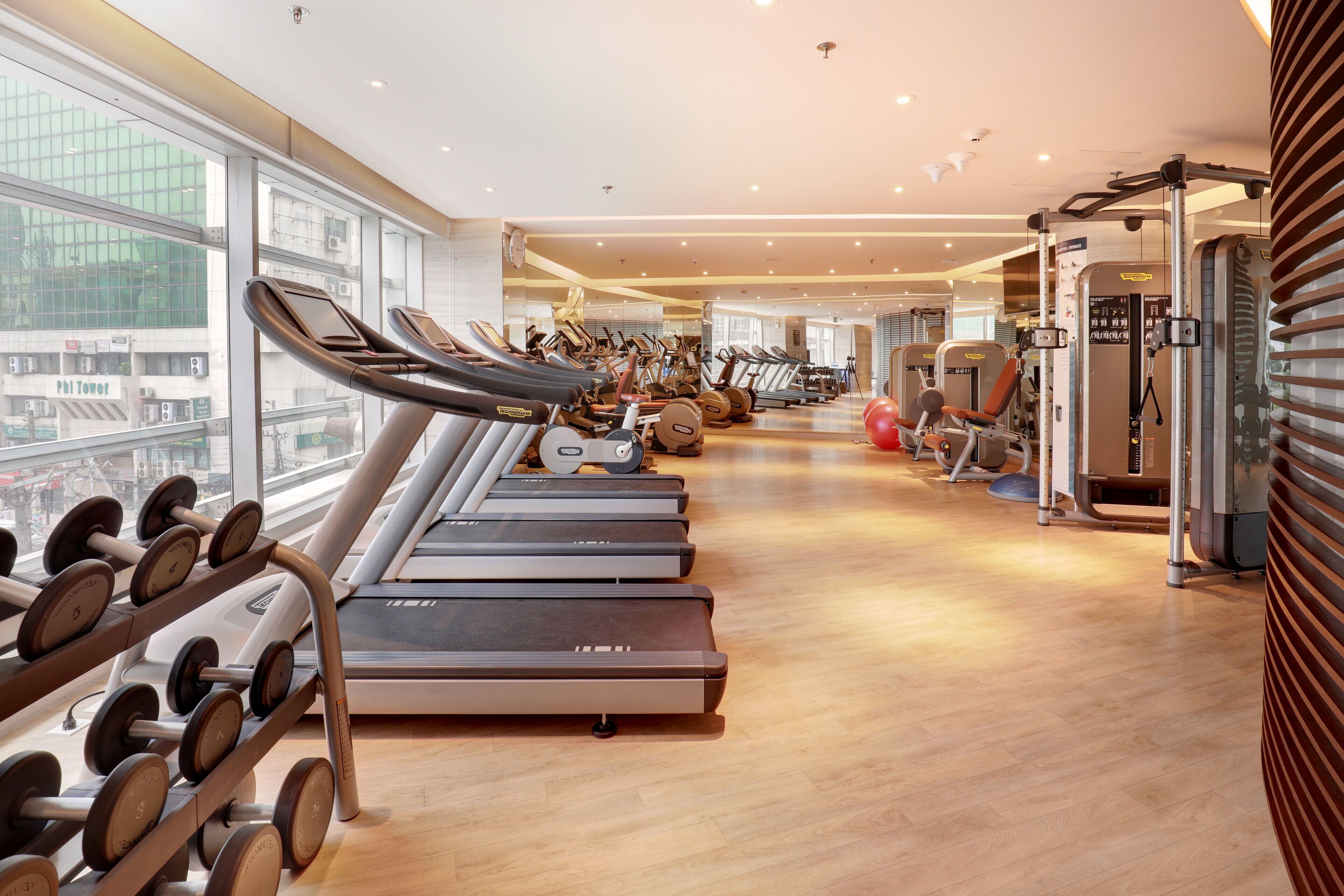 A gym with treadmills, weight machines, and a large window offering a city view.