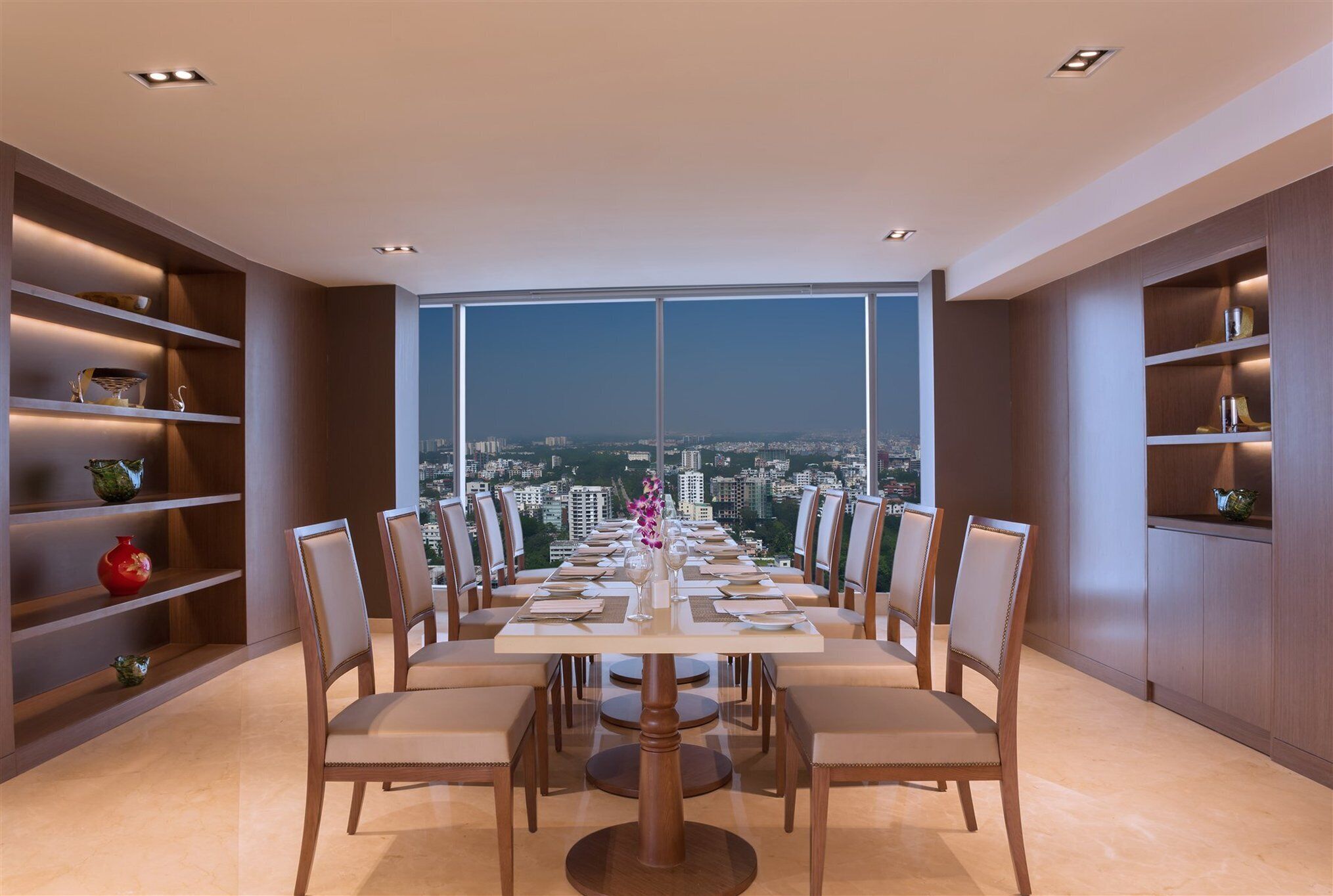 Un espace repas offrant une vue sur la ville, doté de meubles modernes et d’étagères intégrées.