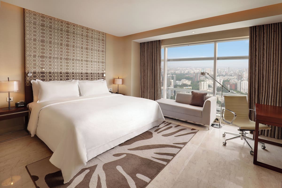 Een moderne hotelkamer met een groot bed, een bank, een bureau met stoel en uitzicht op de stad.