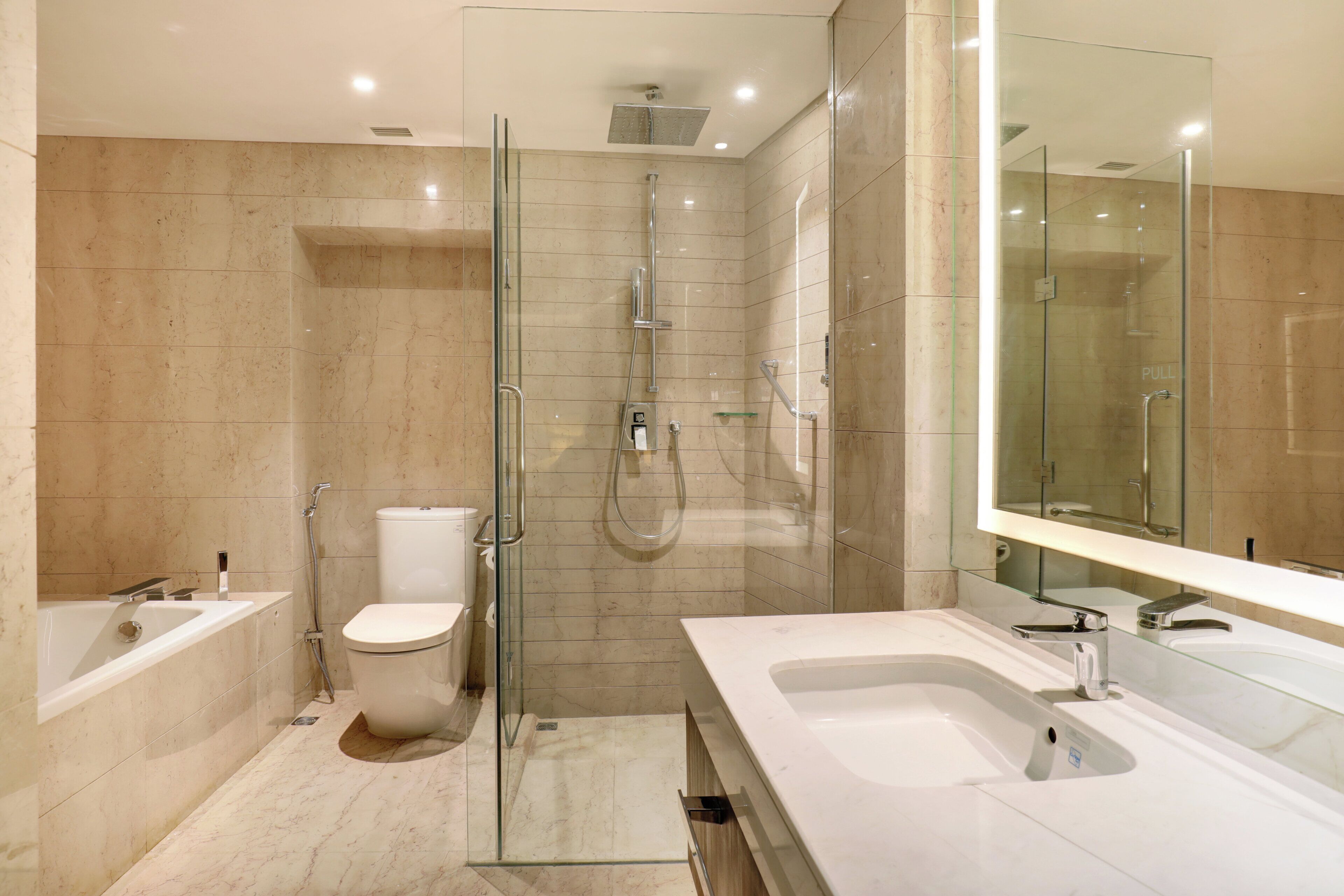 A modern bathroom with a glass-enclosed shower, a toilet, a bathtub, and a large mirror.