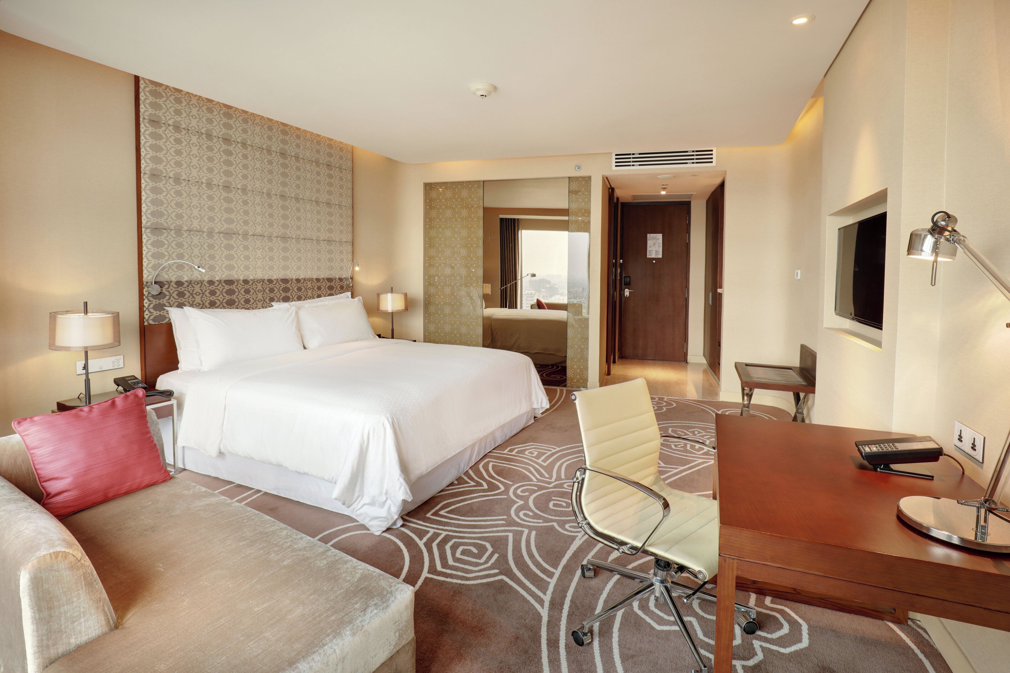 A hotel room with a bed, a desk, a chair, a sofa, and a television.