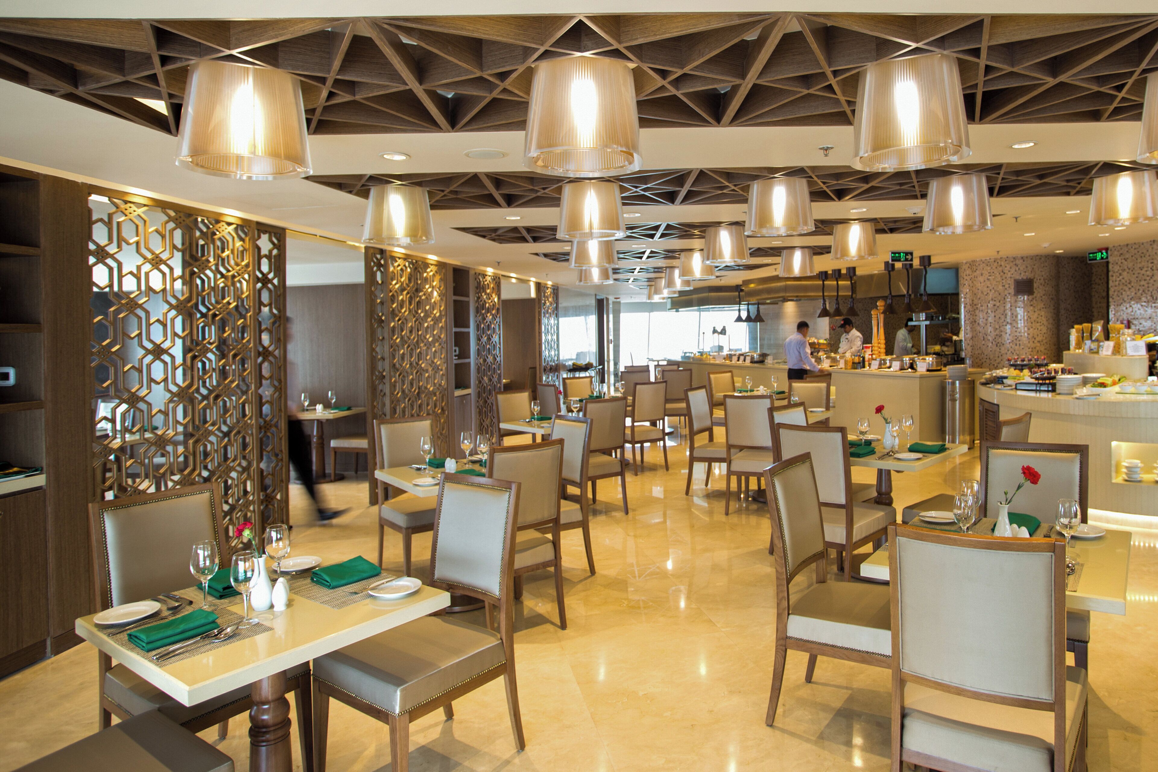 Un interior de restaurante moderno con techos altos, iluminación colgante y una zona de bar central.