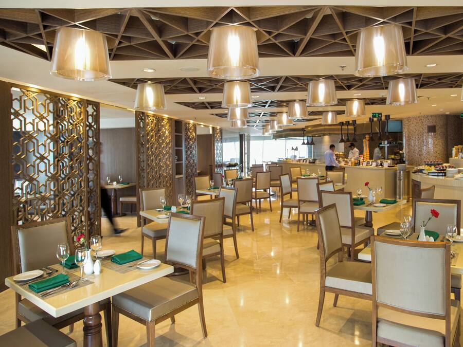 Un interior de restaurante moderno con techos altos, iluminación colgante y una zona de bar central.