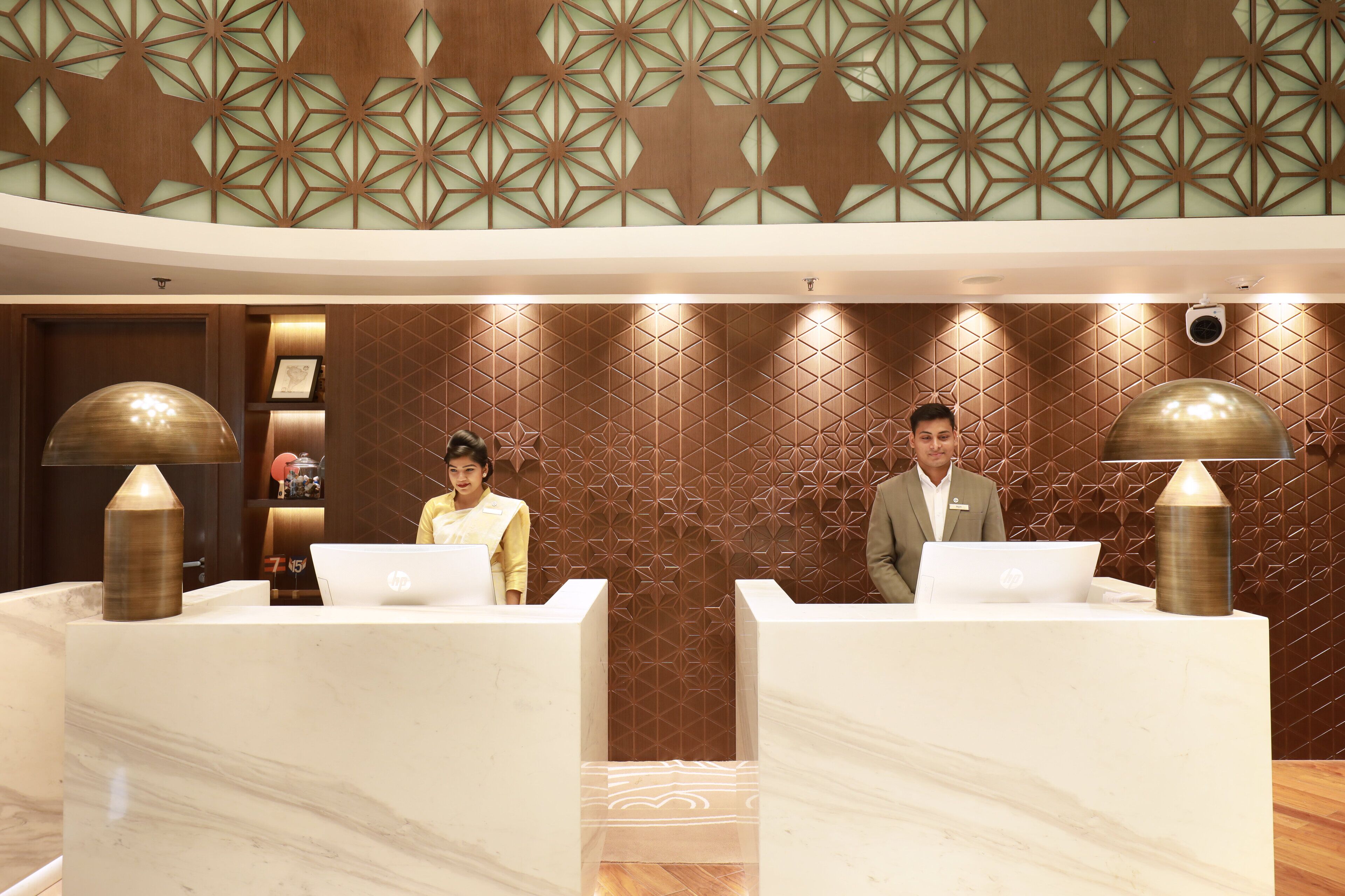 A reception area with marble counters, geometric wall patterns, and two individuals at the reception desk.