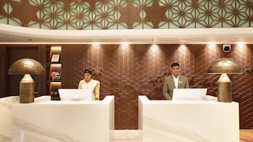 A reception area with marble counters, geometric wall patterns, and two individuals at the reception desk.