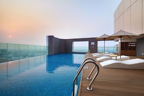 Una piscina infinita con terraza de madera, sillones de descanso y sombrillas.