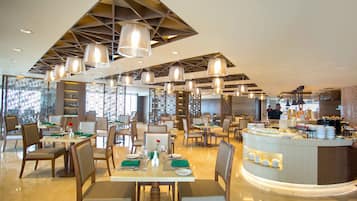 A modern restaurant with multiple dining tables, chairs, and hanging pendant lights.