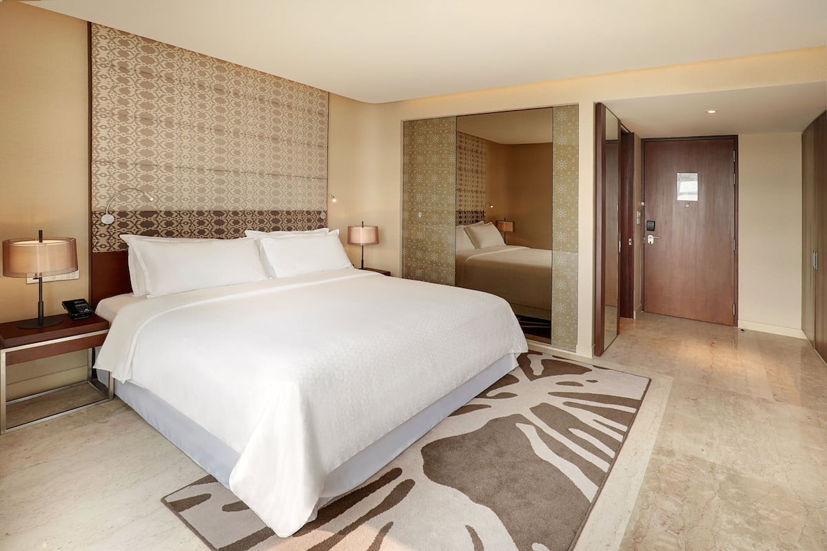 Een hotelkamer met een groot bed, nachtkastjes met lampen, een gestreept hoofdeinde en een spiegel.
