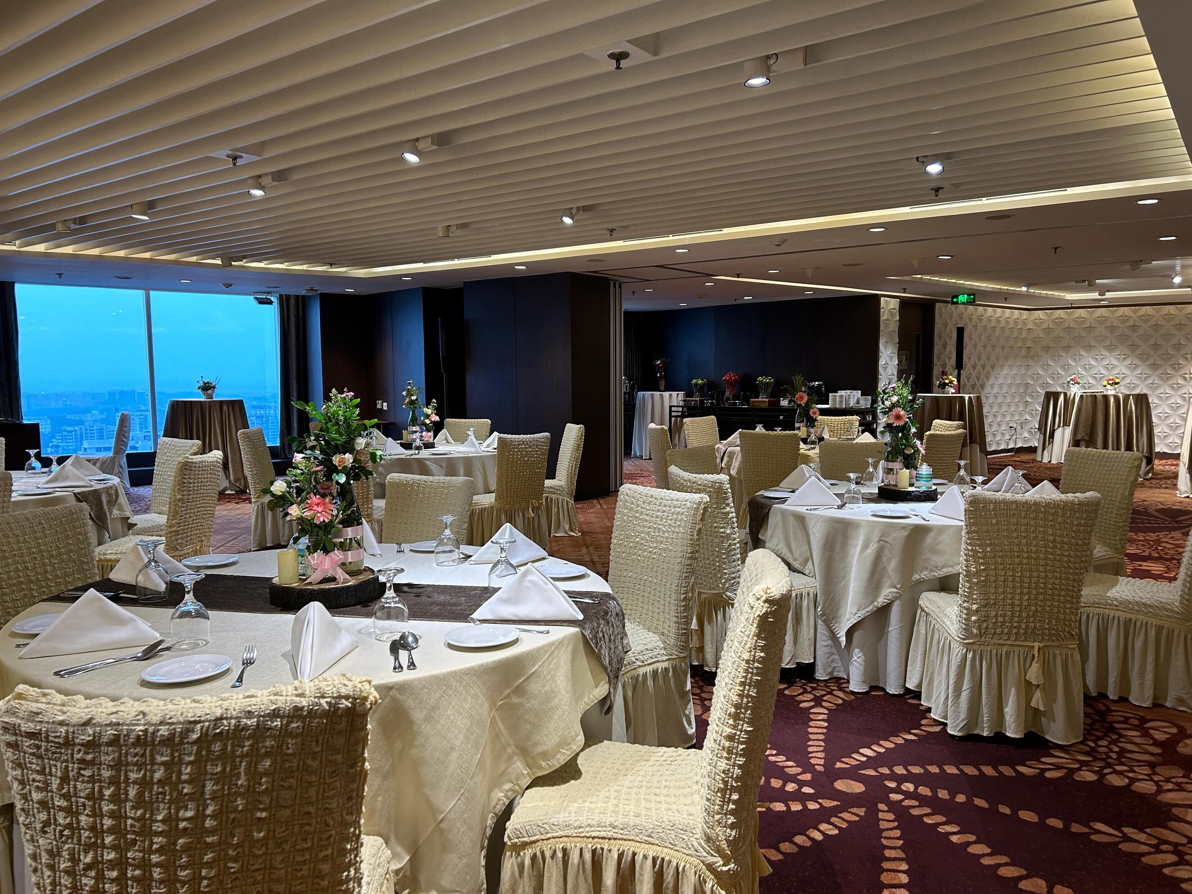 A banquet hall with round tables, white tablecloths, and wicker chairs.