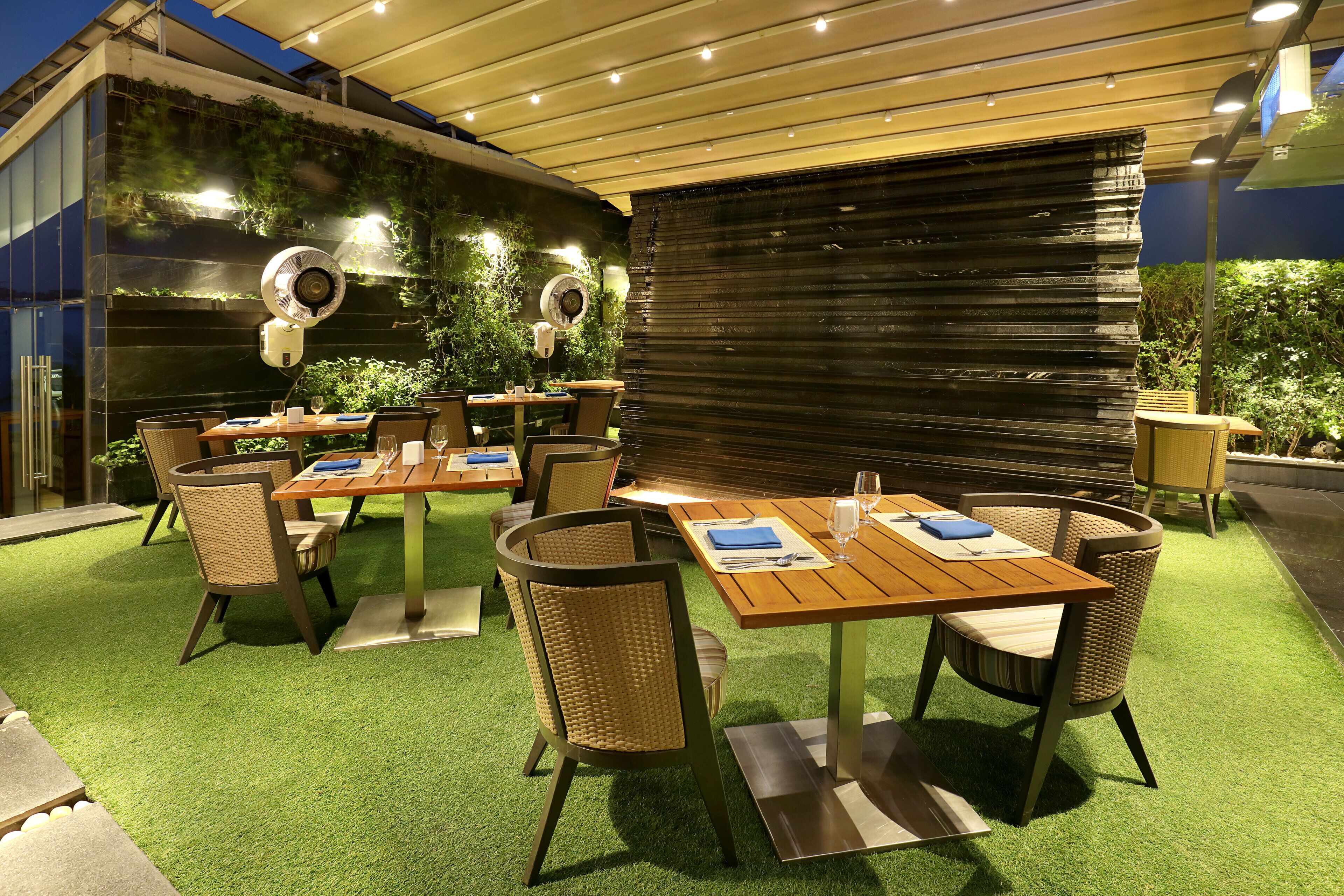 An outdoor dining area with tables and chairs, a pergola, and a wall with climbing plants.