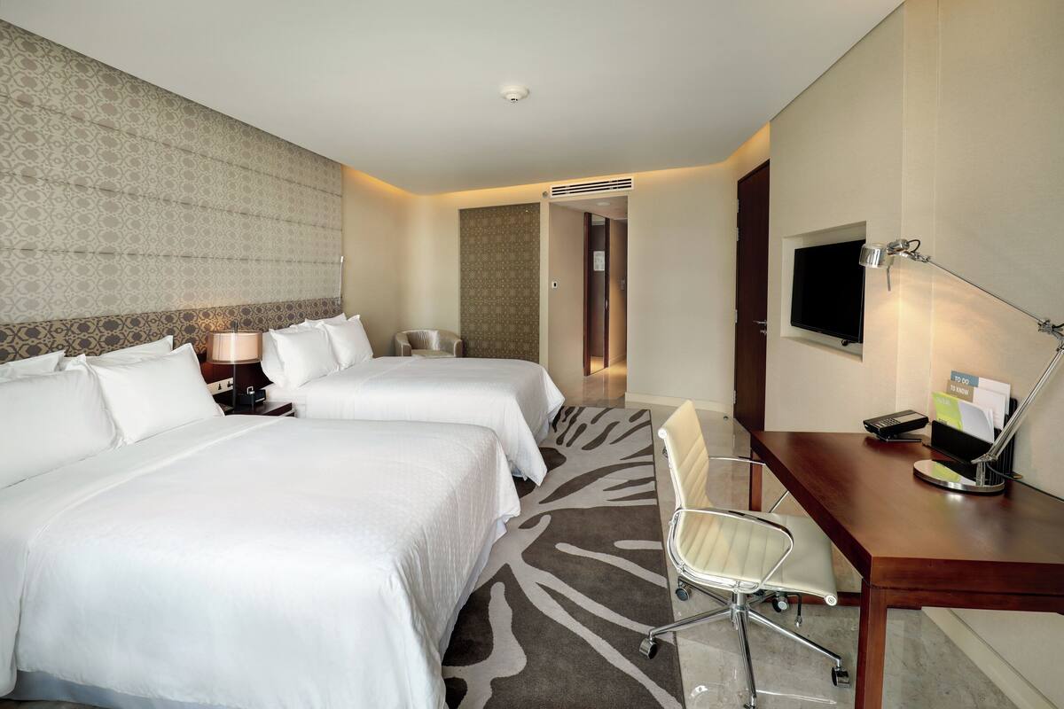 Een hotelkamer met twee bedden, een bureau met stoel, een flatscreen-tv en een kleine tafel met lamp.