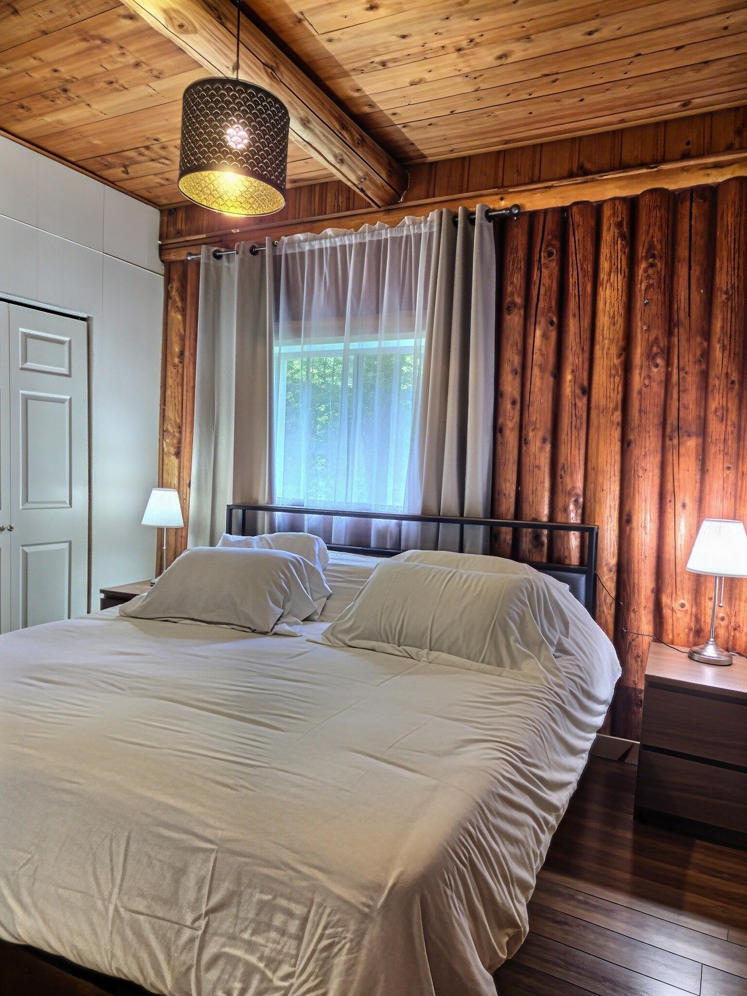 Une chambre avec un plafond en bois, un lit avec une literie blanche, une fenêtre avec des rideaux et deux lampes de chevet.