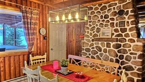 A wooden dining area with a stone wall, a chandelier, and a view of the outdoors. - the Laurentides Private Log and Spa Escape (Rivière-Rouge)