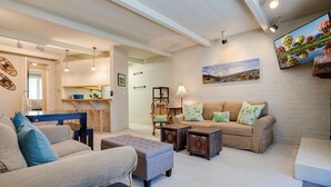 A cozy living room with a sofa, ottoman, and coffee table, a dining area with a table and chairs, and a kitchen in the background. - ST309 | Across the Street from Slopes | Hot Tub | Great location | Free City Bus (Steamboat Springs)