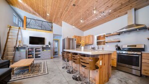 Une cuisine moderne avec des meubles en bois, un îlot central doté de tabourets, un réfrigérateur en acier inoxydable et un four encastré.