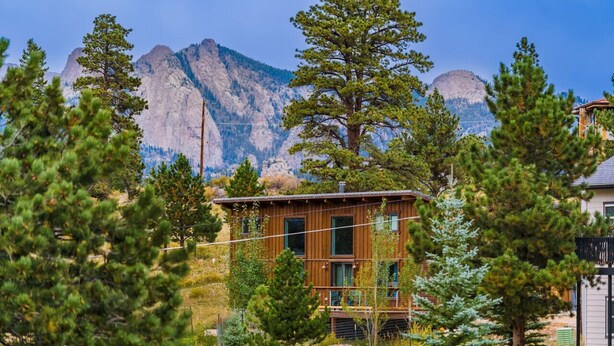 Une cabane aux murs en bois, entourée de pins et située au pied d’une montagne.
