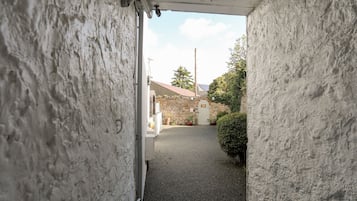 Une ruelle étroite, avec un bâtiment en pierre et un mur blanc d’un côté.